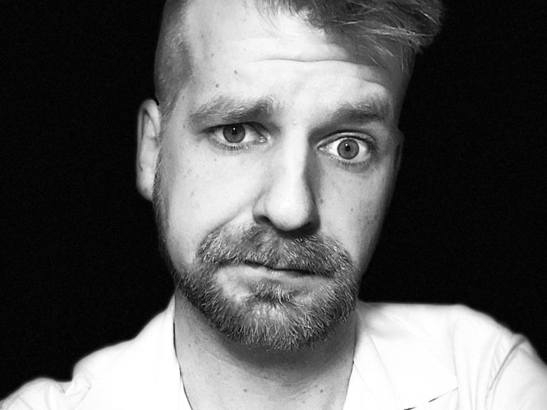 Arty Schulz Portrait Ein Portrait von Arty Schulz im weißen Hemd, mit Vollbart und freundlichem Blick, Haare zur Seite gestylt.